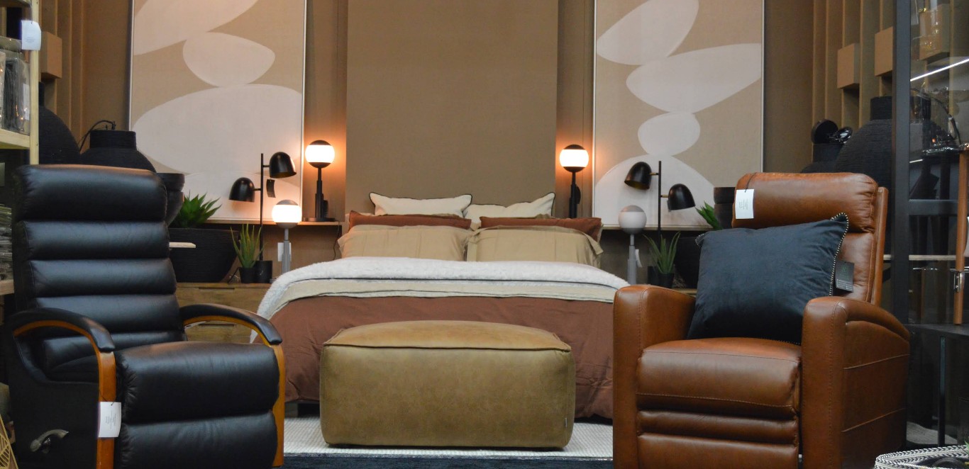A dressed bed flanked by a leather recliner, ottoman and bedside lamps