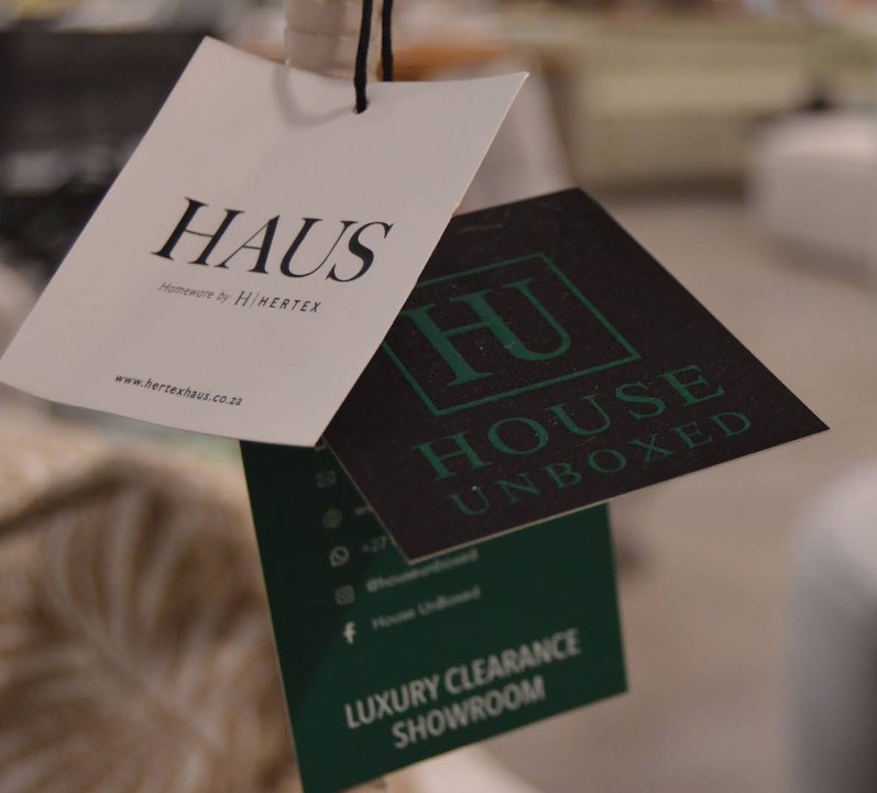 A Hertex HAUS swing tag next to a green House Unboxed clearance tag on a piece of furniture
